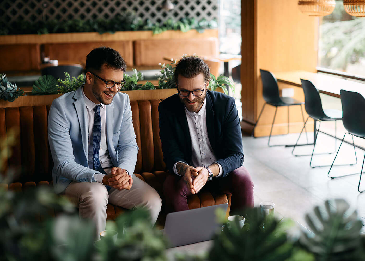 Two men laughing while looking at a laptop in a cafe