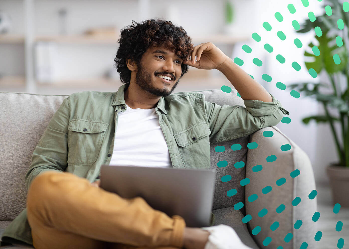 Happy Indian guy in casual sitting on couch with laptop